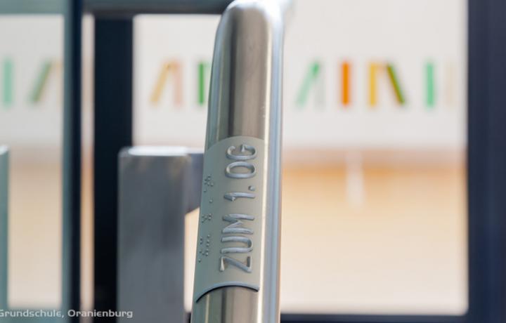 Etagenkennzeichnung durch Handlaufschilder mit Hinweisen zur Standortbestimmung in erhabenen Reliefbuchstaben und in tastbarer Braille-Schrift.